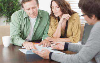A couple reviews home sale paperwork with a real estate agent at a table—featured in a blog about common mistakes sellers make when listing their home.